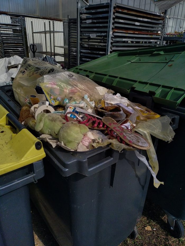 Une poubelle jaune débordante à Mérignac : sacs, jouet en peluche, sandales et emballages posés sur le dessus, sans sac