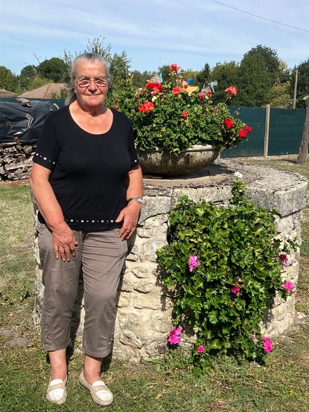 Christianne, debout devant un puits fleuri de géraniums, à Mérignac