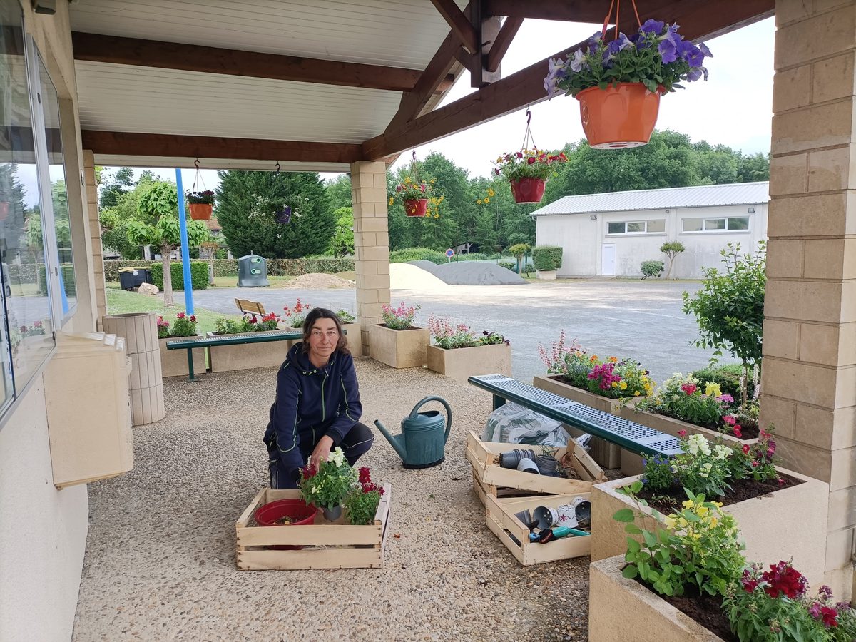 Ingrid, accroupie sous le préau, plante des fleurs dans des jardinières