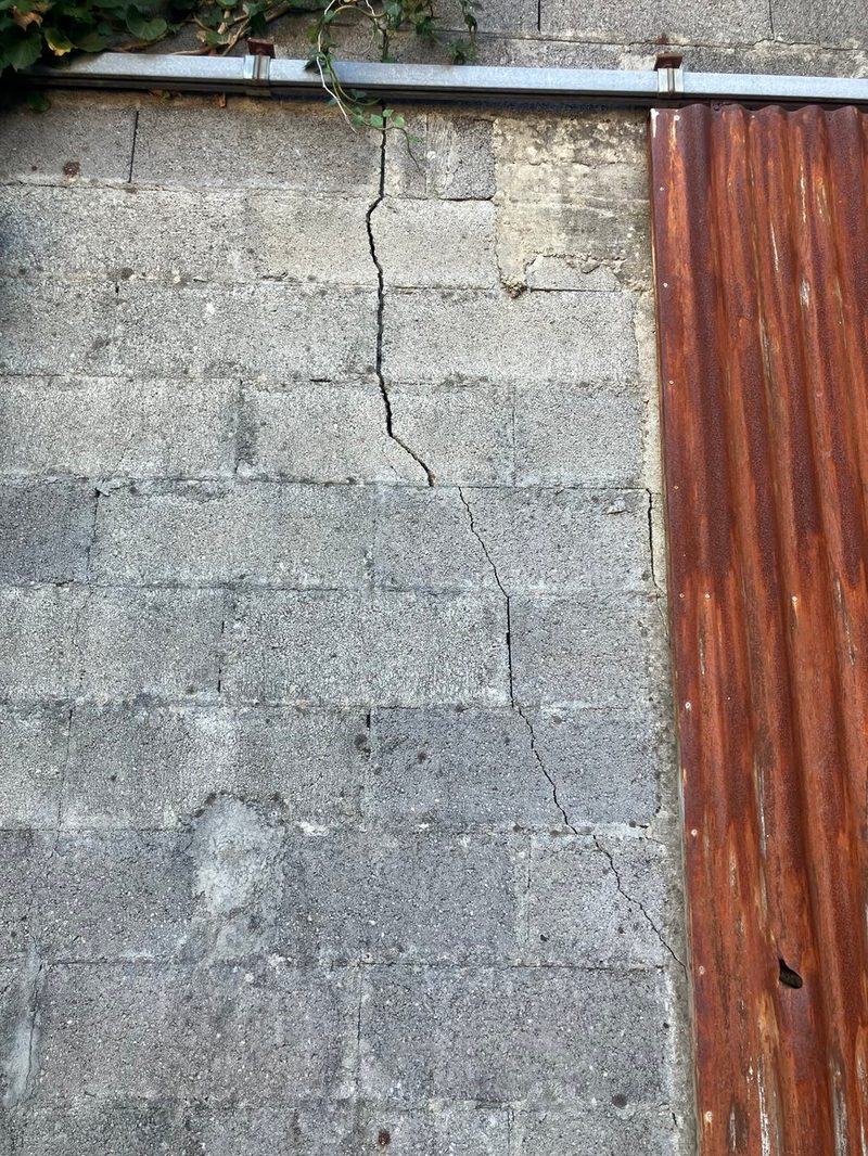 Fissure dans un mur en parpaings, à côté d'une tôle ondulée rouillée